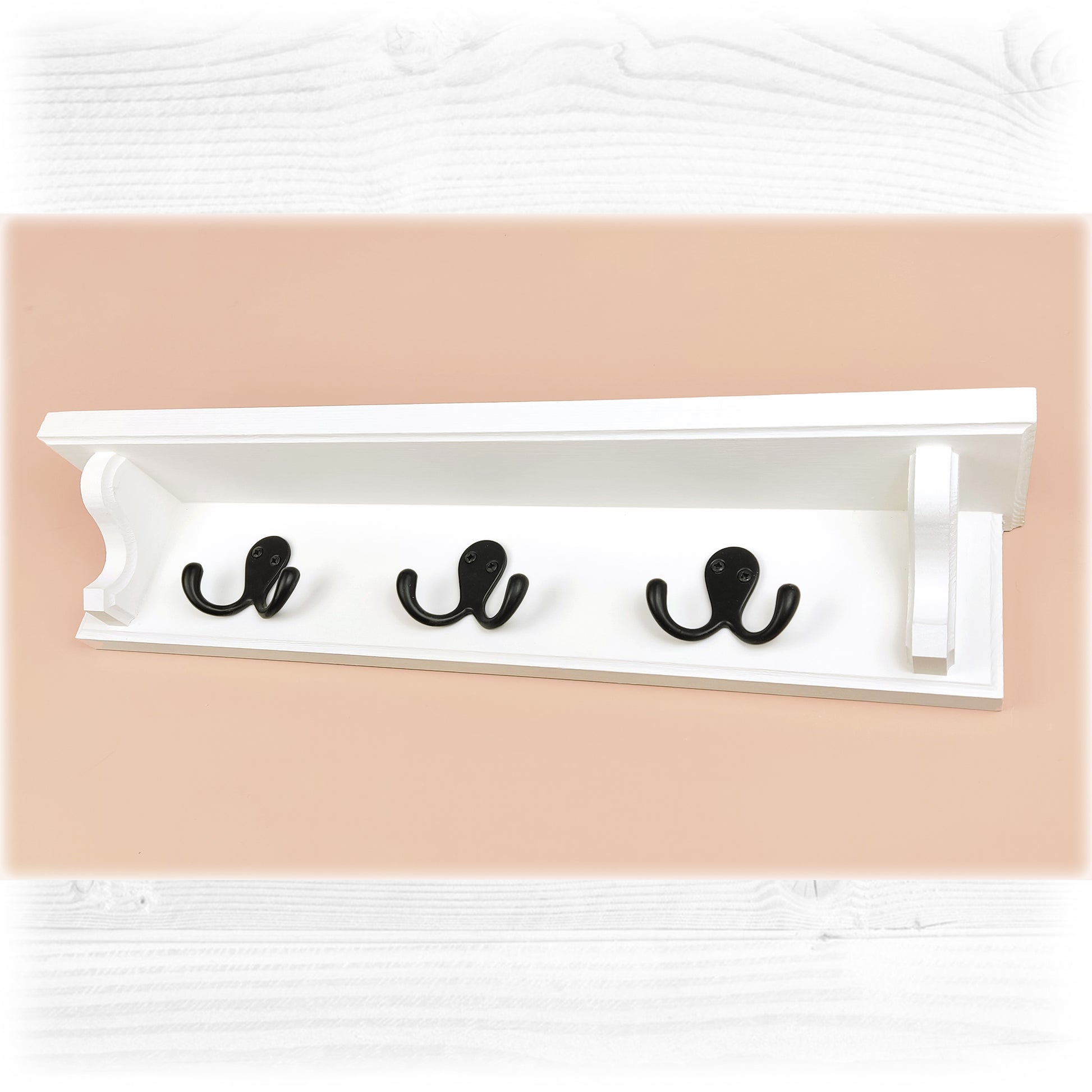 A white wooden floating coak rack with shelf featuring black double coat hooks on a pink background