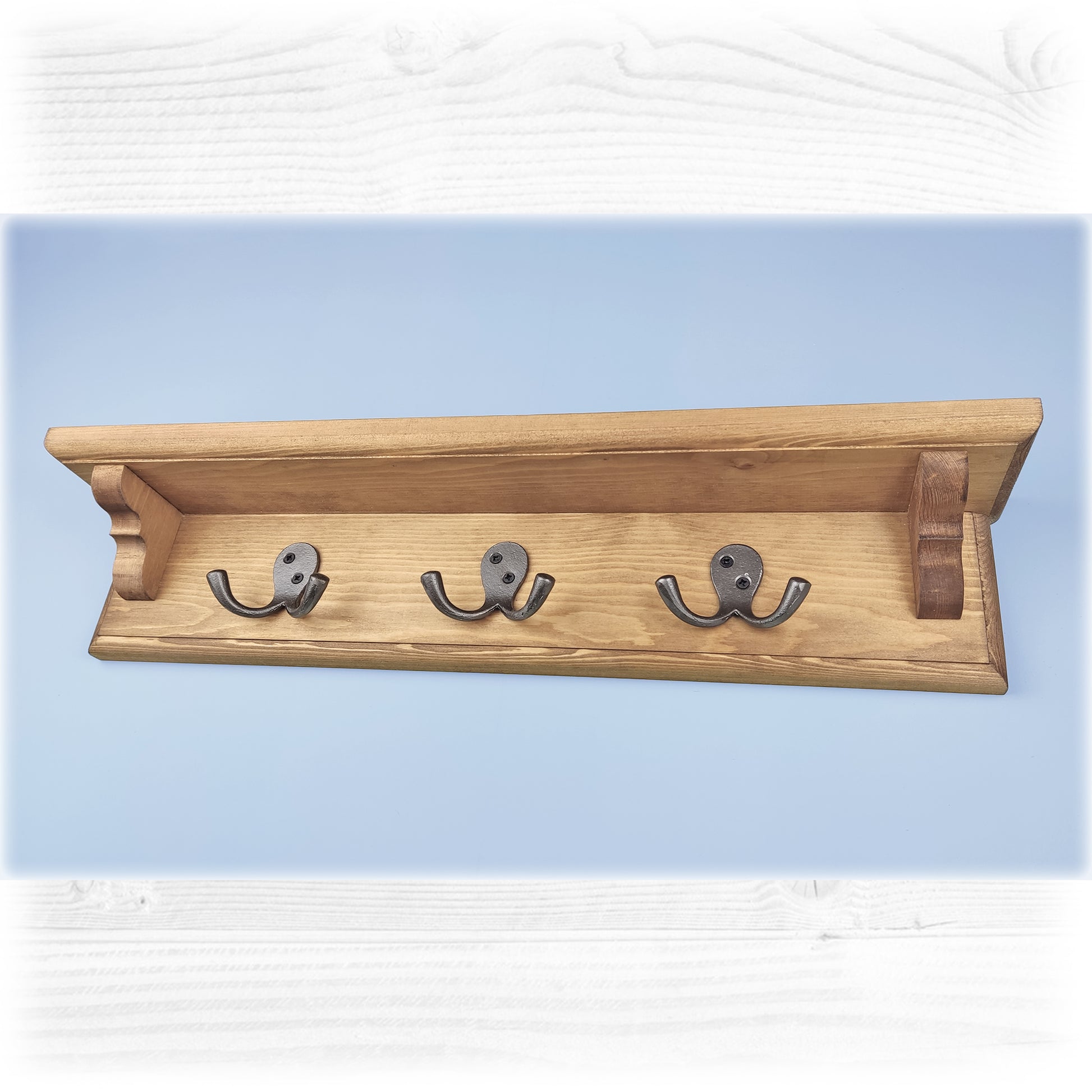 An oak stained wooden floating coat rack with shelf featuring cast iron double coat hooks on a blue background