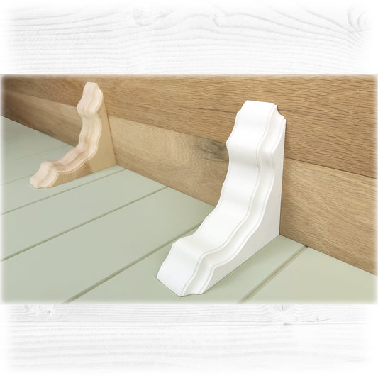 A pair of solid wooden corbels one unfinished in a natural light wood colour and the other in a chalk painted white and finished with a wax seal holding up an oak shelf on a green cladded background