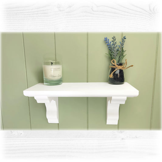 A chalk painted white wooden floating shelf with a green cladded background