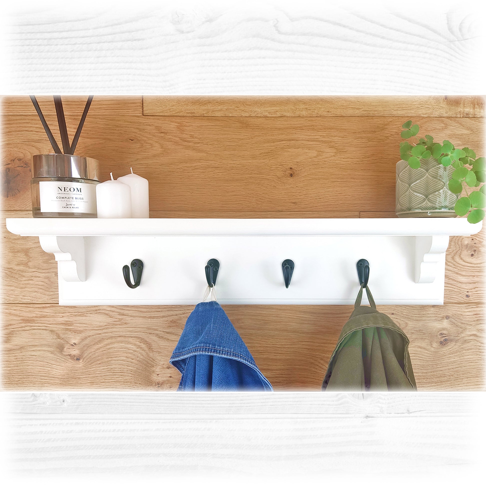 A white wooden floating coat rack with shelf on an oak wooden background featuring black coat hooks