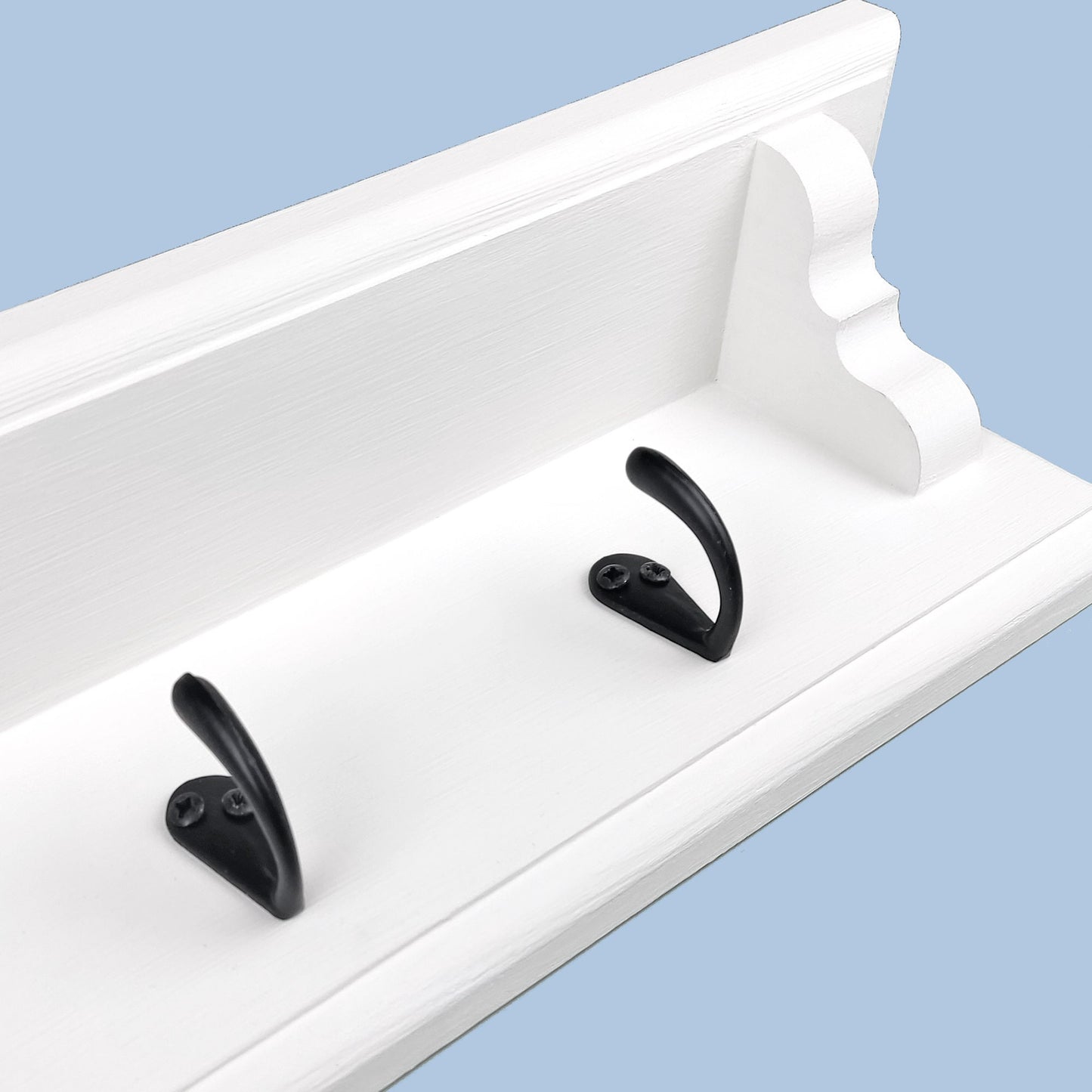 A close up on a solid wooden hite chalk painted coat rack with black coat hooks on a blue background